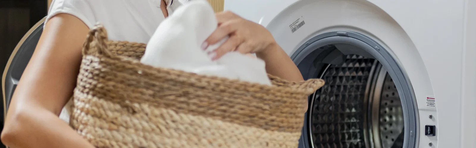 Iemand tilt een wasmand naast een wasmachine