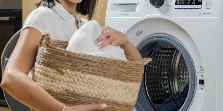 Iemand tilt een wasmand naast een wasmachine
