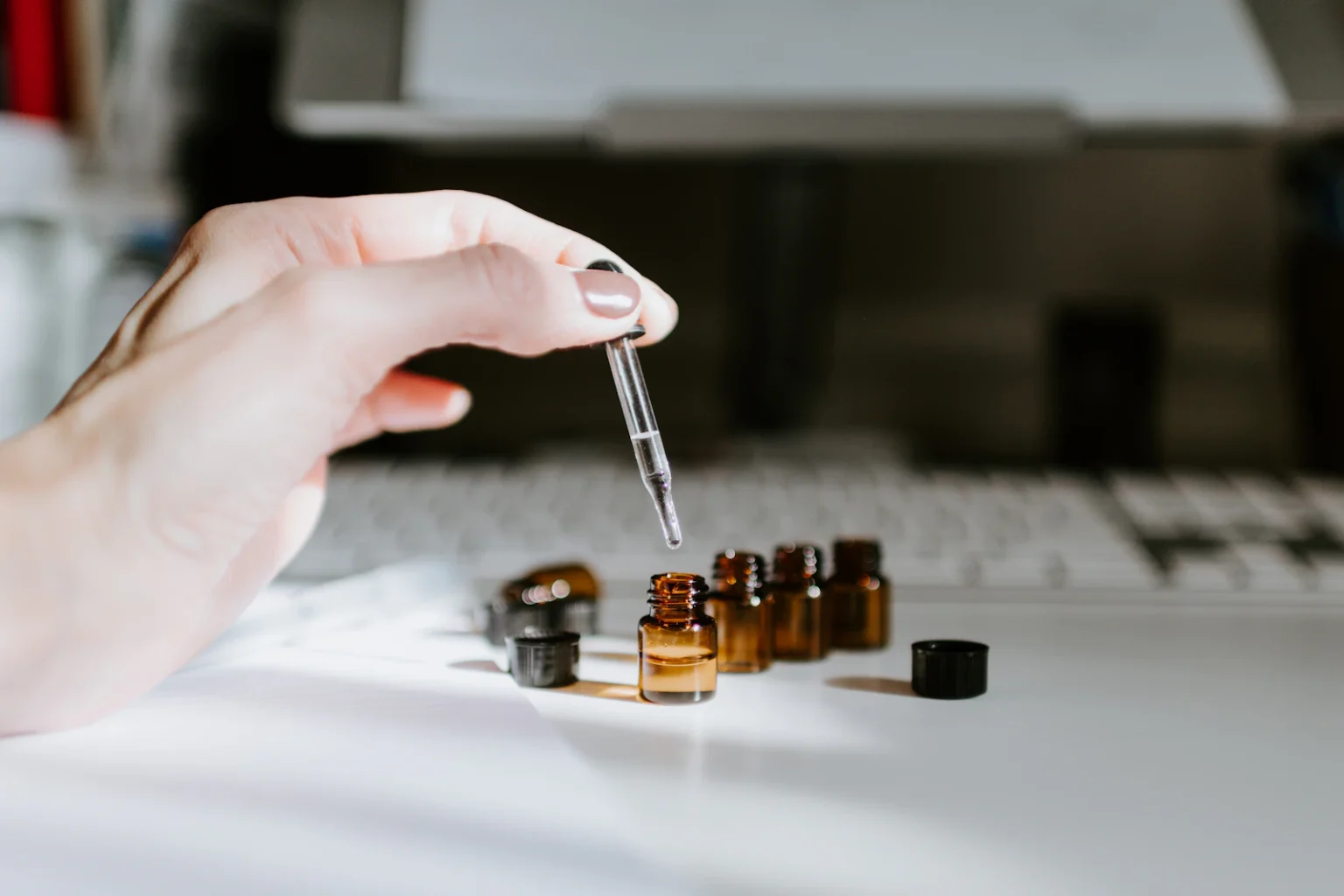 Een hand met een pipet boven kleine glazen flesjes
