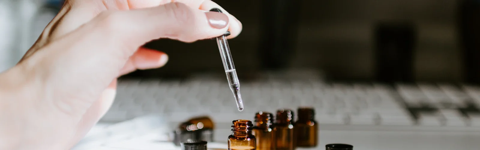 Een hand met een pipet boven kleine glazen flesjes