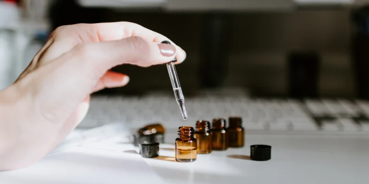 Een hand met een pipet boven kleine glazen flesjes
