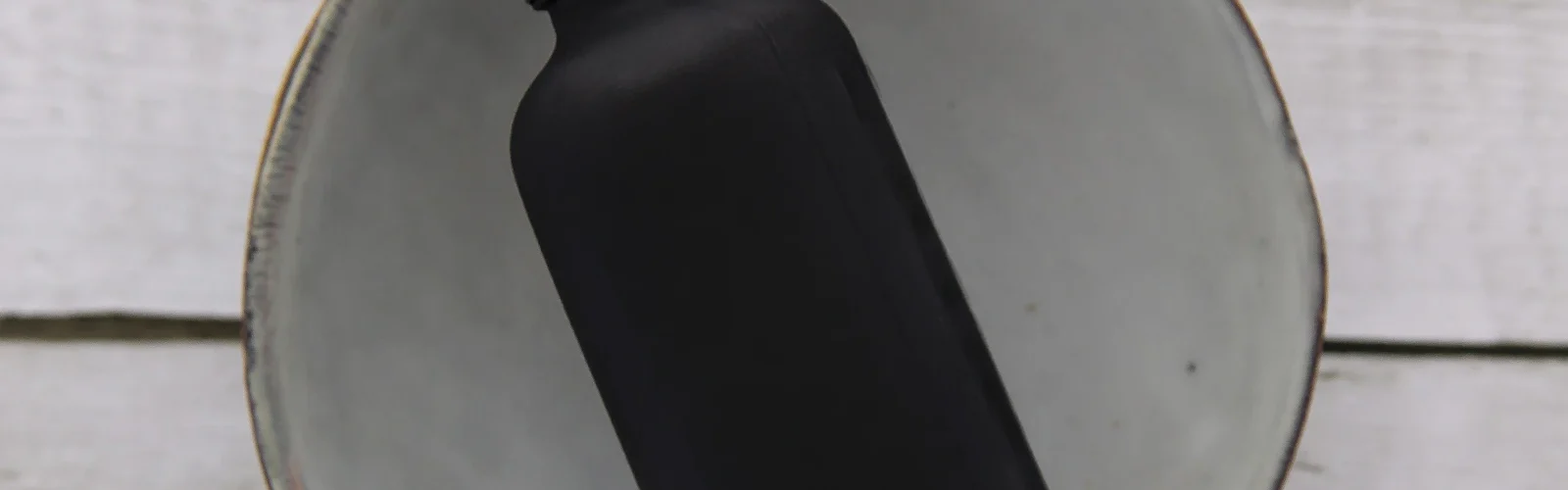 Een klein flesje met een pipetdop op een lichte houten plank