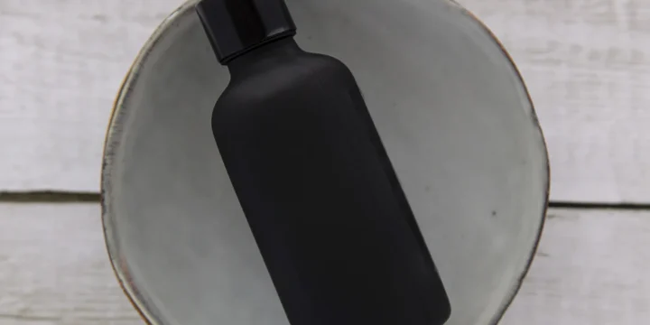 Een klein flesje met een pipetdop op een lichte houten plank