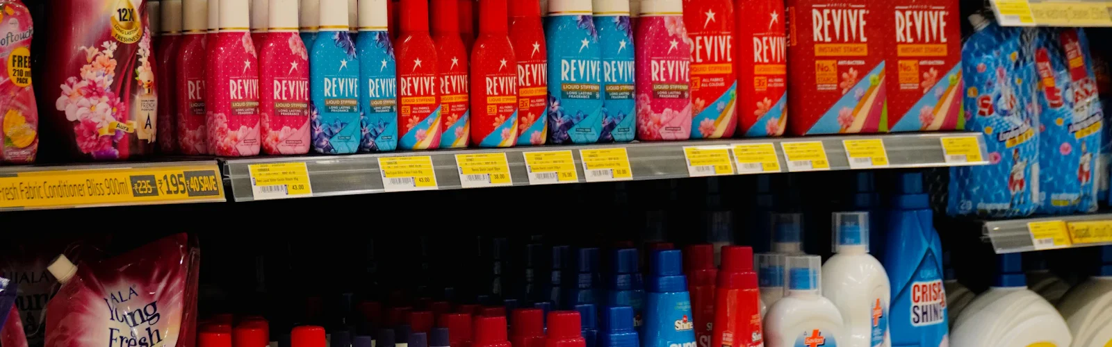 Een winkelschap vol flessen wasmiddel met prijskaartjes eronder