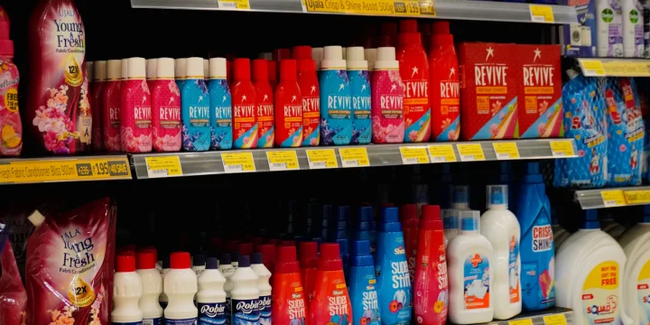 Een winkelschap vol flessen wasmiddel met prijskaartjes eronder